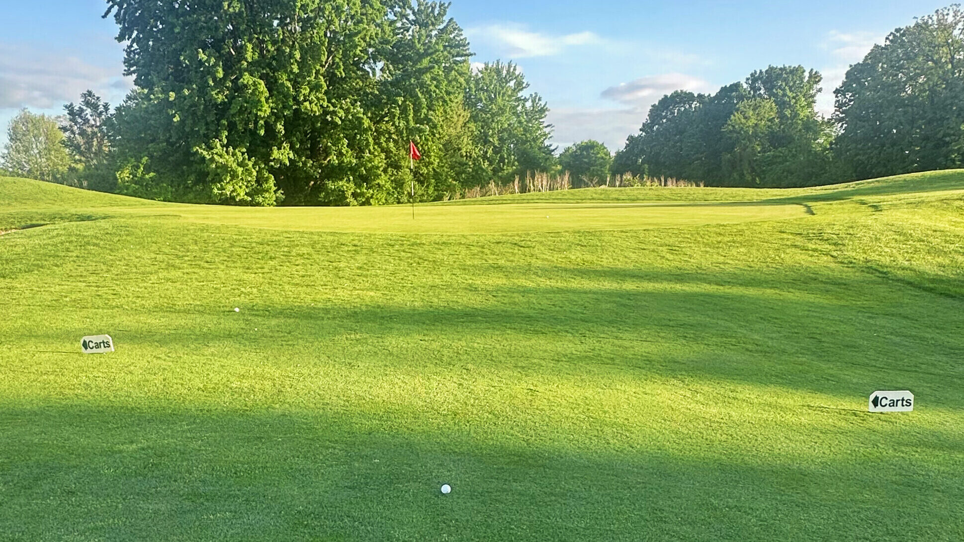 Golf ball resting in the apron short of the green on Hole 7 at Fellows Creek, framed by evening light and a clear view of the flagstick.