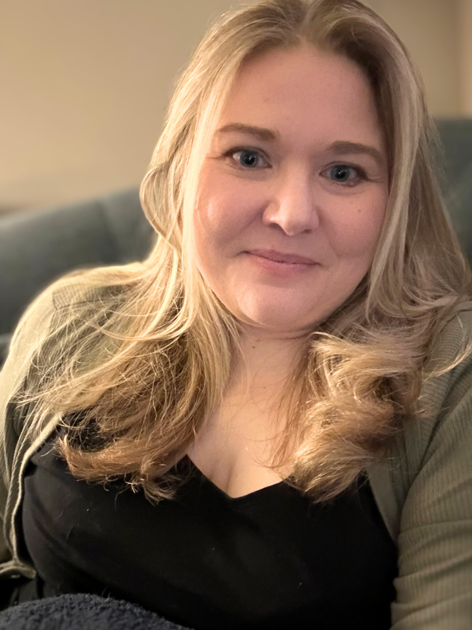 Close-up of Julie sitting indoors, smiling gently with relaxed hair and a casual sweater