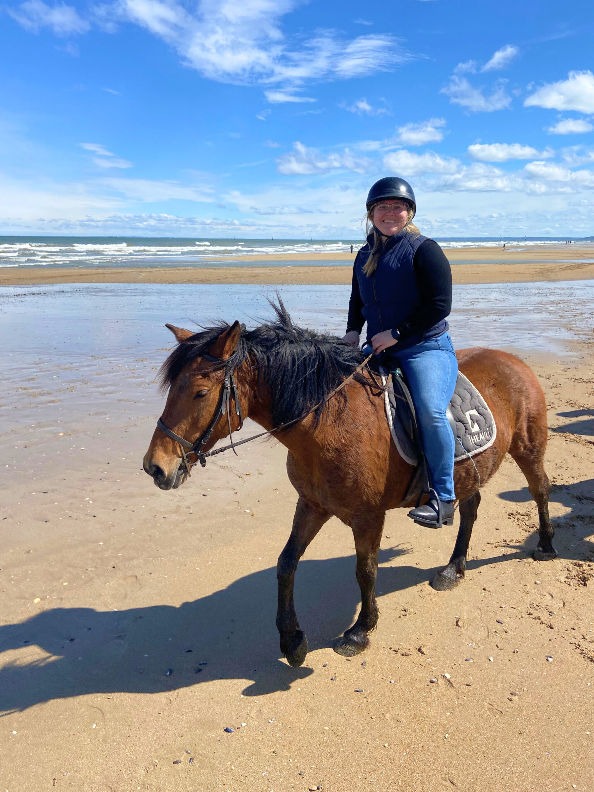 Woman horseback riding along a sandy beach with ocean waves in the background.